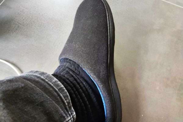 Pied chaussé d’un chausson noir sur sol gris.