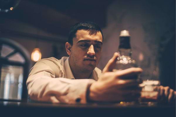 Homme observe une bouteille d’alcool au bar.