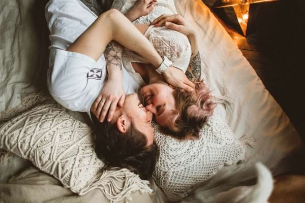 Deux amoureux rient et s’enlacent tendrement dans un lit cosy.