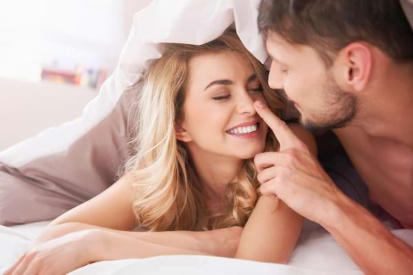 Couple complice sous la couette, sourire et tendresse.