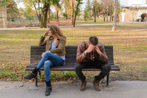 Un couple en froid sur un banc, chacun regarde ailleurs.