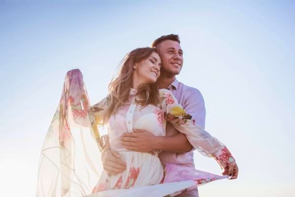 Un couple heureux s’enlace sous un ciel bleu ensoleillé.