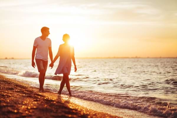 Un couple marche main dans la main sur la plage au coucher de soleil.