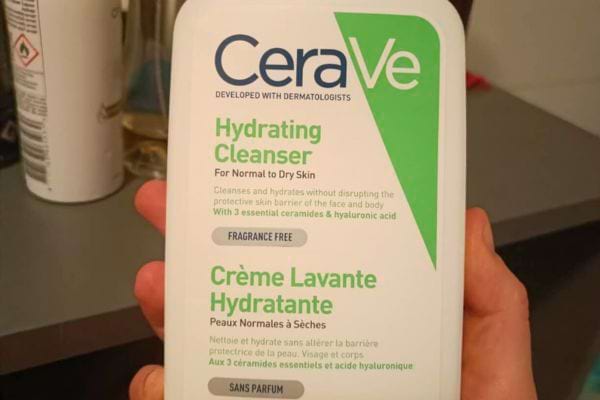 Un flacon de crème lavante hydratante CeraVe est tenu en main.