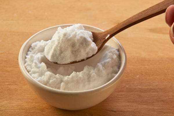 Une cuillère en bois contenant du bicarbonate blanc au-dessus d’un bol.