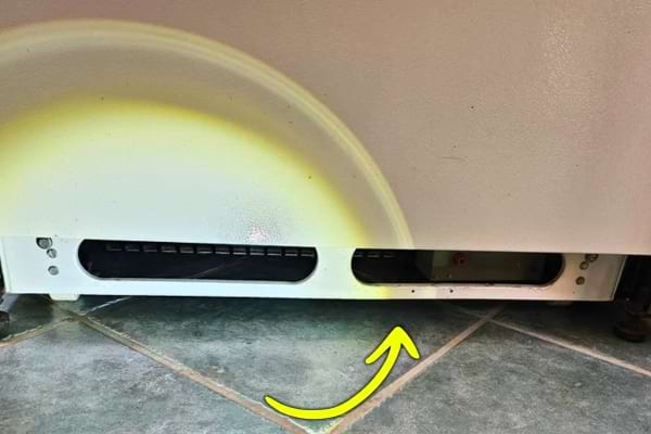 Vue du bas d’un frigo avec une flèche jaune pointant vers la grille d’aération.