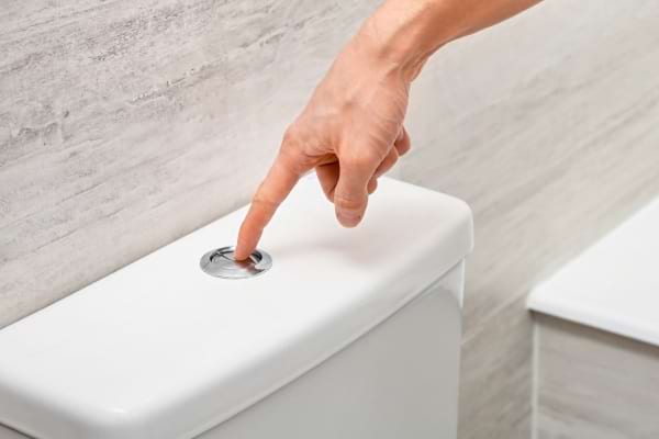 Un doigt appuie sur un bouton de chasse d’eau encastré dans un mur.