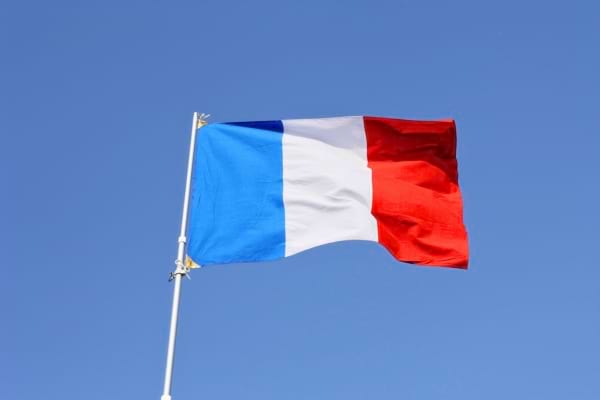 Un drapeau français flotte fièrement dans le ciel bleu, bien tendu par le vent.