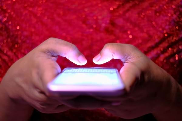 Mains tapant un message sur un téléphone avec fond rouge brillant.