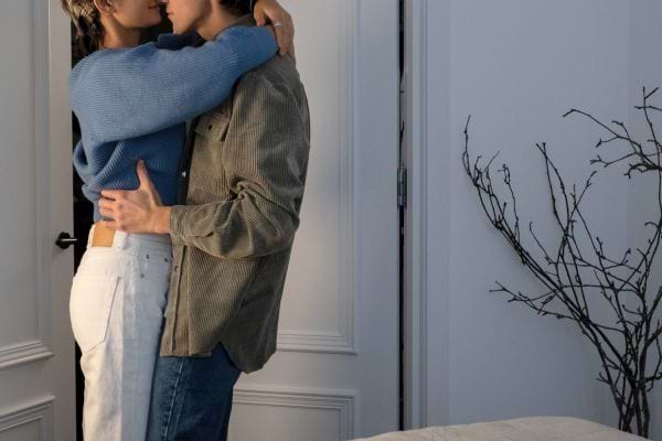 Un couple debout s’étreint dans une pièce intime.