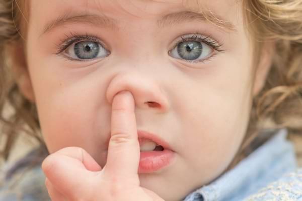 Une petite fille se cure le nez du doigt avec un air surpris.