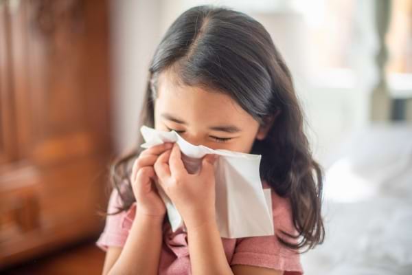 Une petite fille se mouche avec un mouchoir en papier.