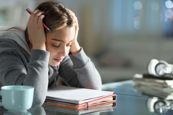 Une jeune femme semble épuisée en travaillant, la tête dans ses mains au-dessus de ses cahiers.
