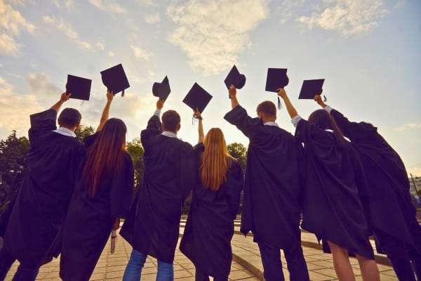 Des étudiants en toge célèbrent leur remise de diplômes en levant leurs chapeaux.