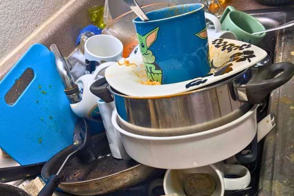 Vaisselle très entassée avec mugs, assiettes et poêles sales.