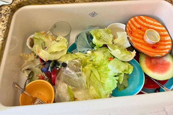 Évier envahi de salades, épluchures et vaisselle sale.
