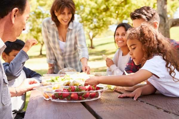 Famille réunie autour d’un pique-nique en plein air, souriante et partageant un repas convivial sous les arbres.