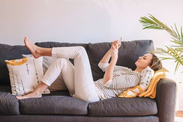 Een vrouw ligt ontspannen op de bank en gebruikt haar telefoon.