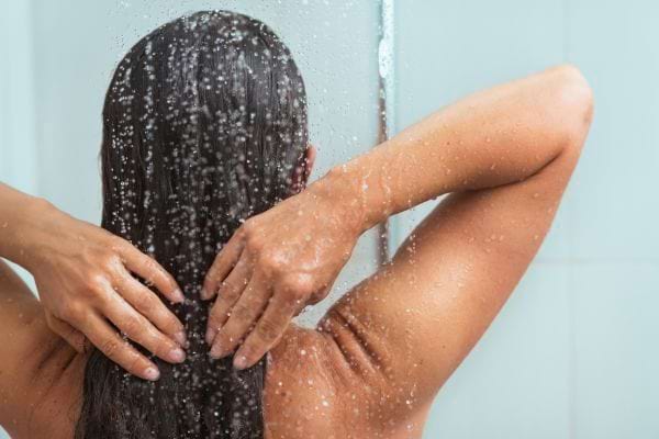 Une femme mouille ses cheveux sous l’eau en tenant sa tête.