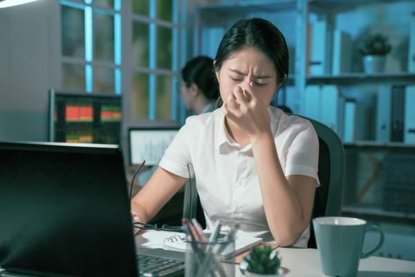 Jeune femme fatiguée, assise devant un ordinateur, se pince l’arête du nez.