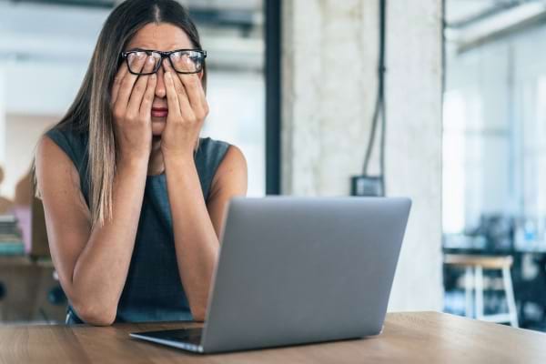 Une femme fatiguée se frotte les yeux devant son ordinateur, signe de troubles du sommeil ou d'épuisement.