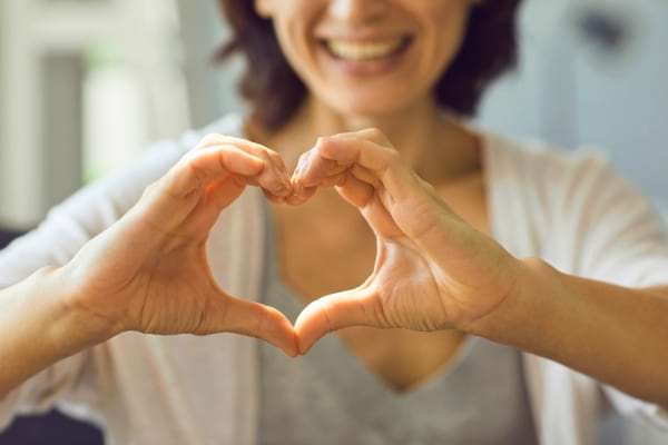 Une femme sourit et forme un cœur avec ses mains devant elle.