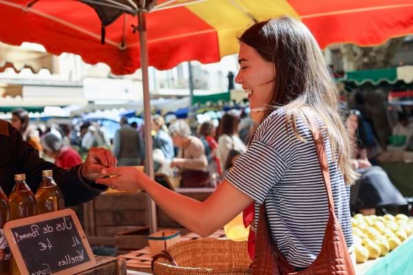 Jeune femme souriante en train de payer sur un marché en plein air.