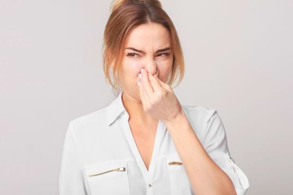 Une femme pince son nez avec une expression de dégoût face à une mauvaise odeur.