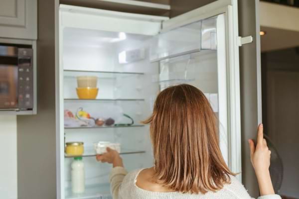 Une femme regarde l’intérieur presque vide de son frigo, hésitante.