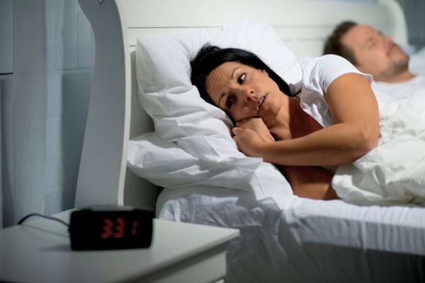 Une femme éveillée regarde l’heure pendant que son compagnon dort.