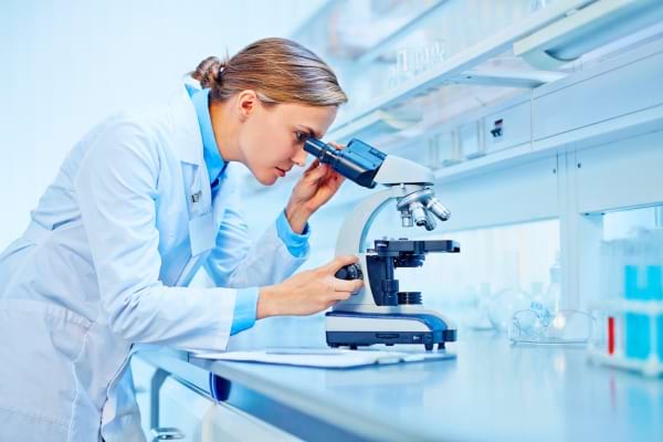 Femme en blouse blanche observant dans un microscope dans un laboratoire moderne, symbole de recherche scientifique.