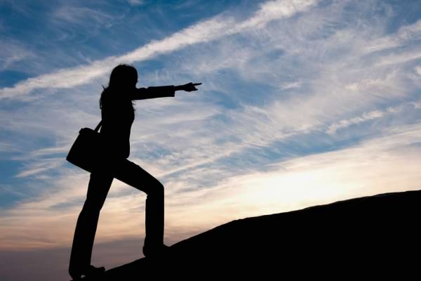 Silhouette d’une femme pointant au loin sur une colline au coucher du soleil.