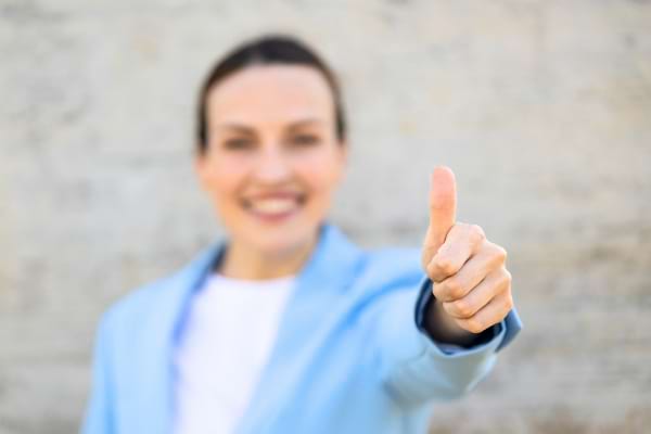 Femme souriante faisant un pouce levé, geste symbolisant l’approbation, la satisfaction ou l’accord.