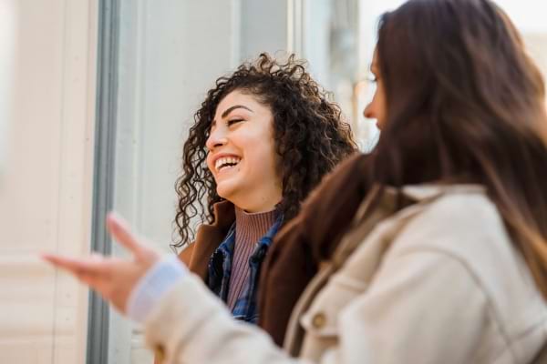 Deux femmes discutent et rient ensemble dans la rue, visiblement complices.