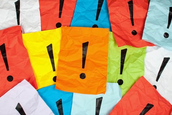 Feuilles de papier colorées, froissées, avec un point d’exclamation noir au centre de chacune.