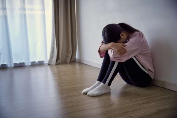Une jeune fille est assise seule au sol, la tête dans les bras.
