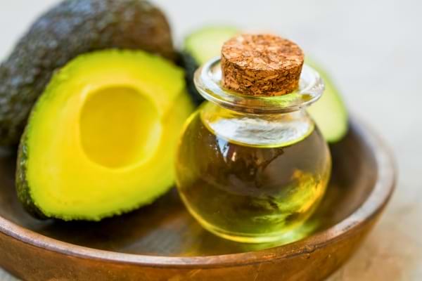 Flacon en verre rempli d’huile d’avocat devant un avocat ouvert.