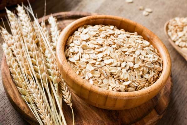 Flocons d’avoine dans un bol en bois, posés près d’épis de blé.