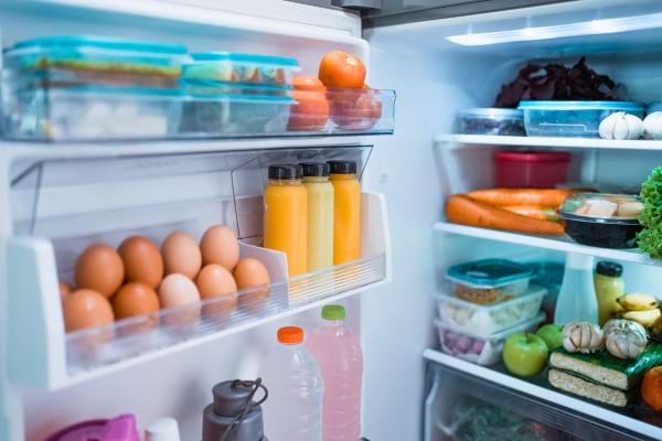 Un frigo bien rempli avec jus, légumes, œufs et boîtes hermétiques soigneusement rangées.