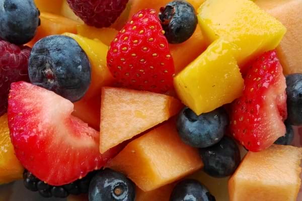 Un gros plan coloré de fruits frais coupés : fraises, myrtilles, mangue, melon.