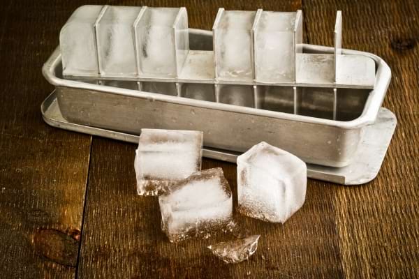 Des glaçons dans un bac en métal, posés sur une table en bois.