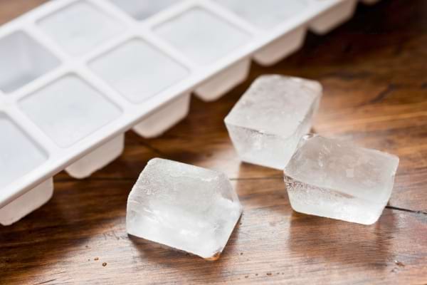 Trois glaçons devant un bac en plastique blanc sur une surface en bois.