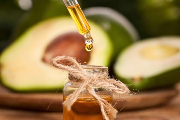 Pipette versant une goutte d’huile dans un petit flacon devant des avocats.