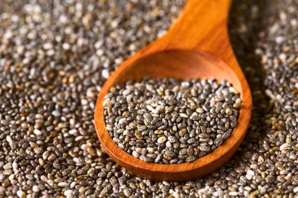 Graines de chia dans une cuillère en bois sur fond de graines.