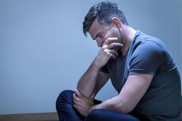 Un homme seul au sol, pensif, la main sur la bouche.