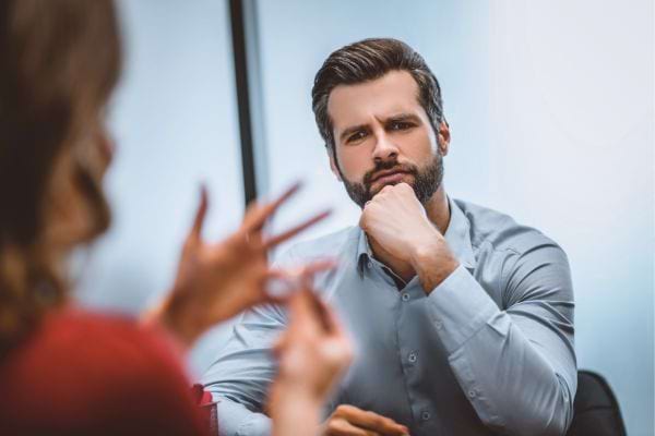 Un homme pensif &eacute;coute une femme qui parle avec ses mains.