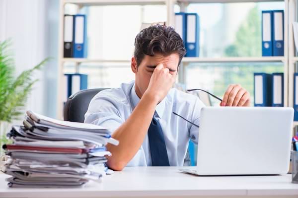 Employé épuisé au bureau, la tête dans la main, papiers empilés à côté.