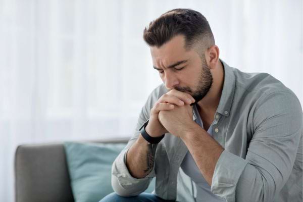 Un homme en chemise grise, yeux fermés, l’air tourmenté.