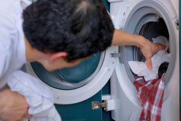 Un homme insère des vêtements dans le tambour de sa machine.