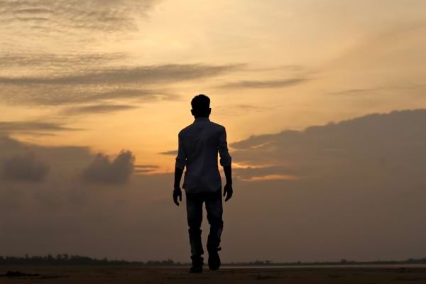 Homme vu de dos, marchant seul sur une plage au coucher du soleil.